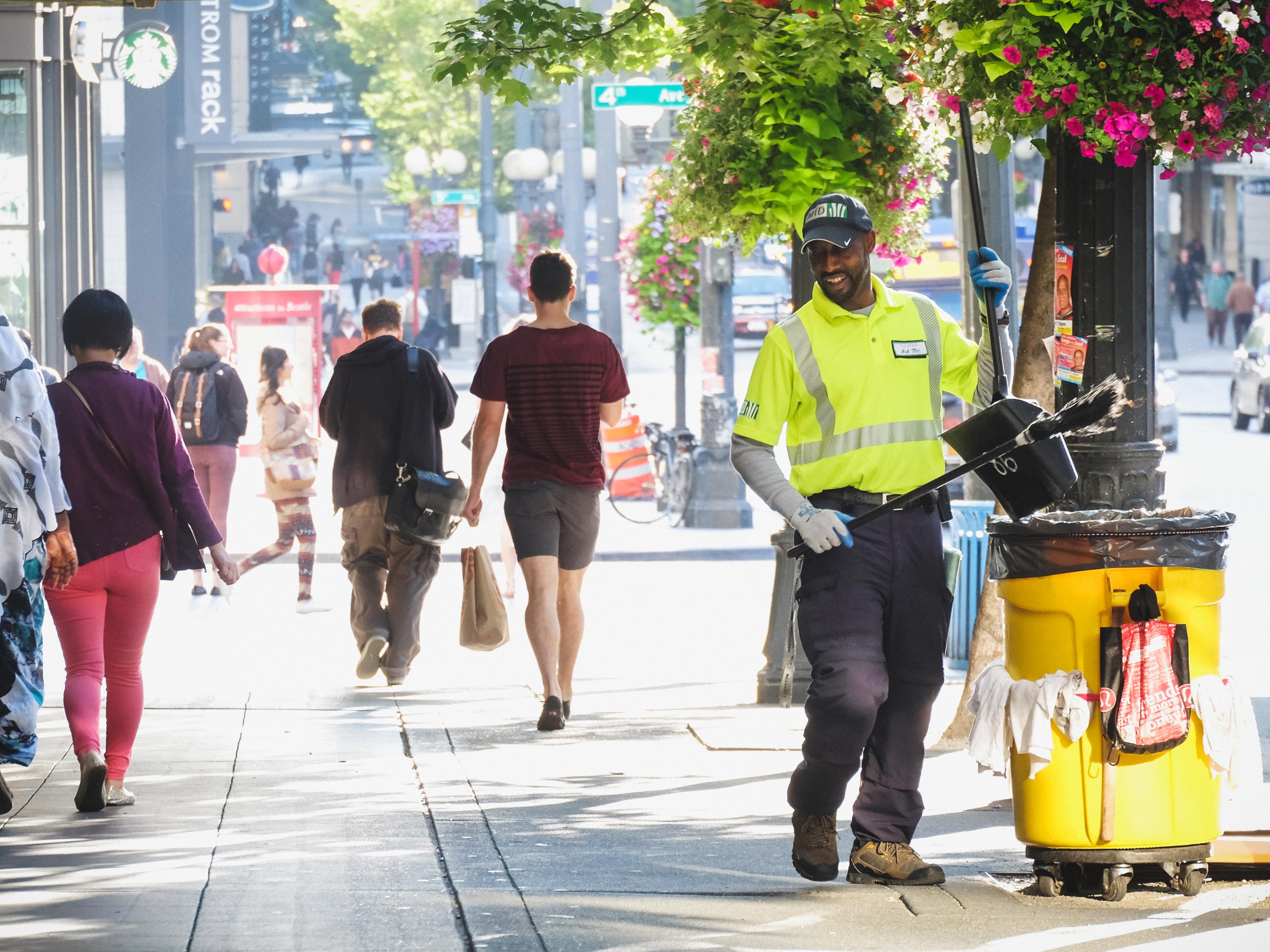 Smiling man walks down a sunny street with a trash can