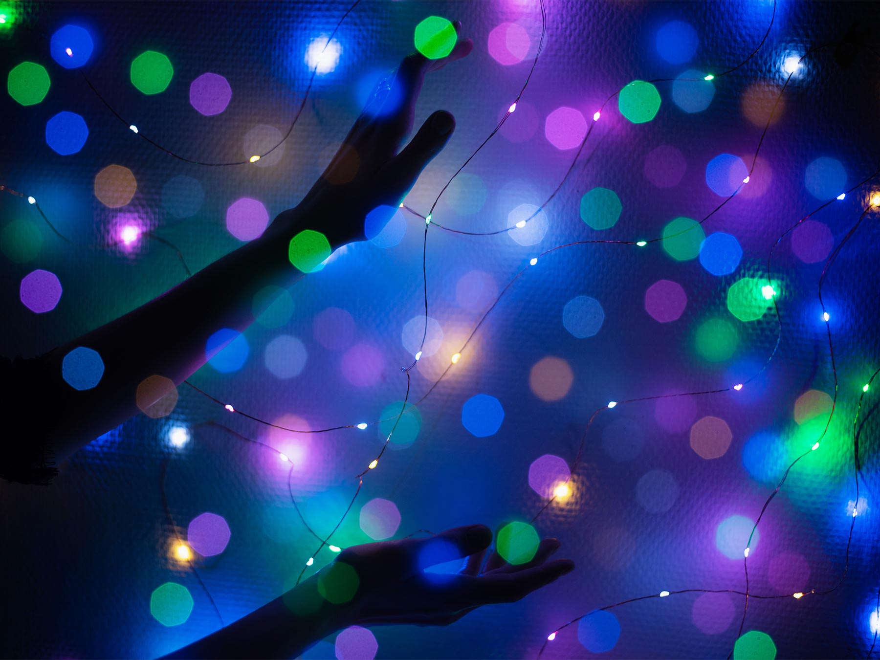 Holiday lights, hand reaching out, blue background with magenta, green, blue and orange lights