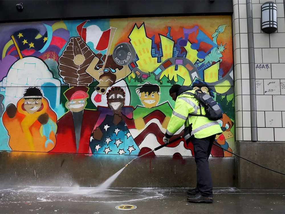 Downtown ambassador power washing sidewalk in front of a colorful mural in downtown Seattle