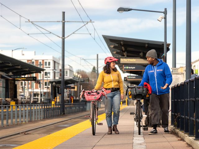Two people walking their bikes and talking at a light rail station