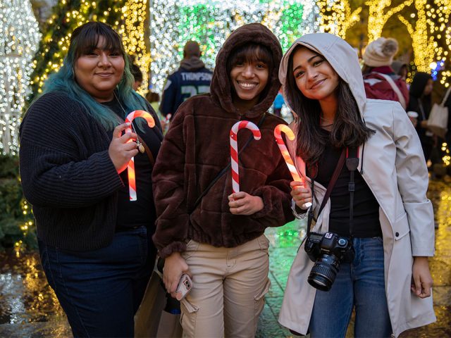 Three friends smiling with glow stick candy canes and holiday lights at Westlake Park in downtown Seattle