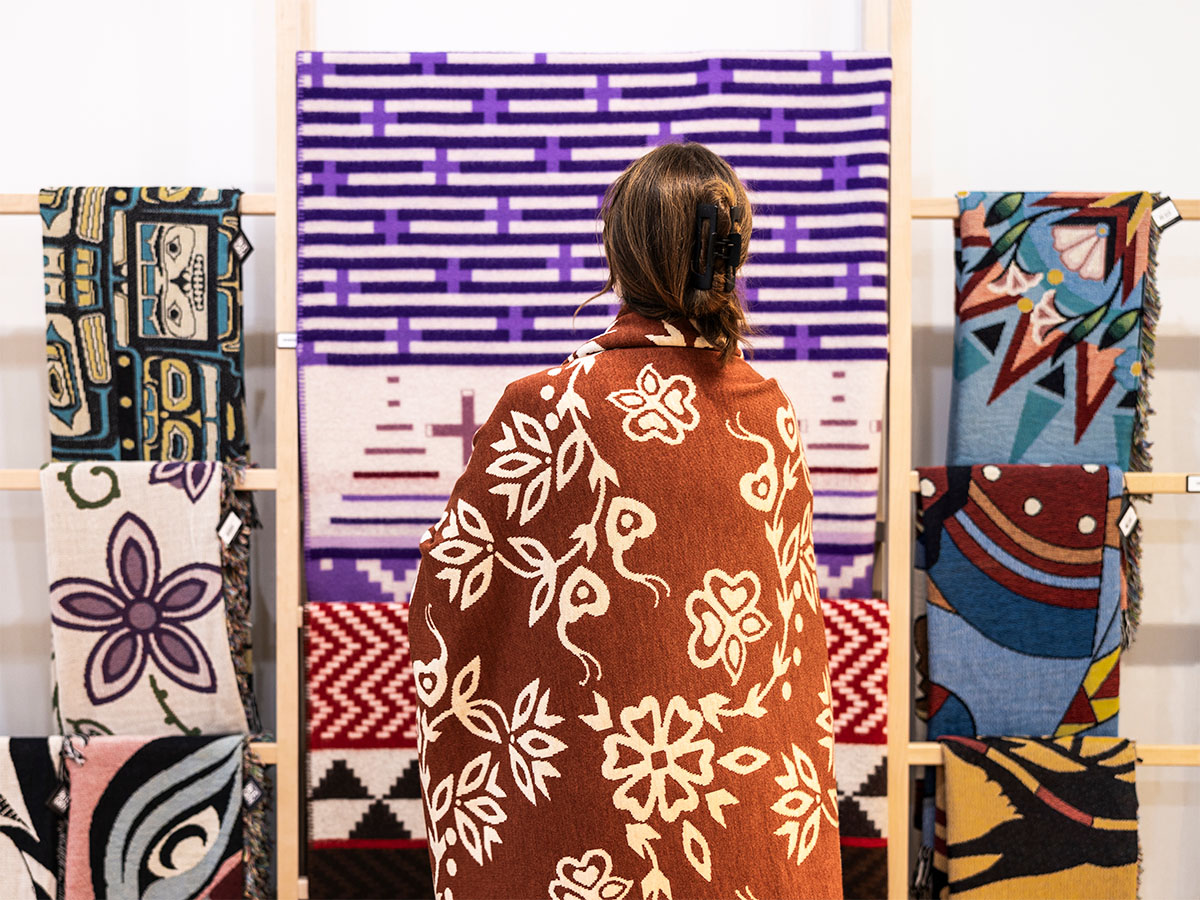 Woman wearing blanket looking at a wall of bright blankets