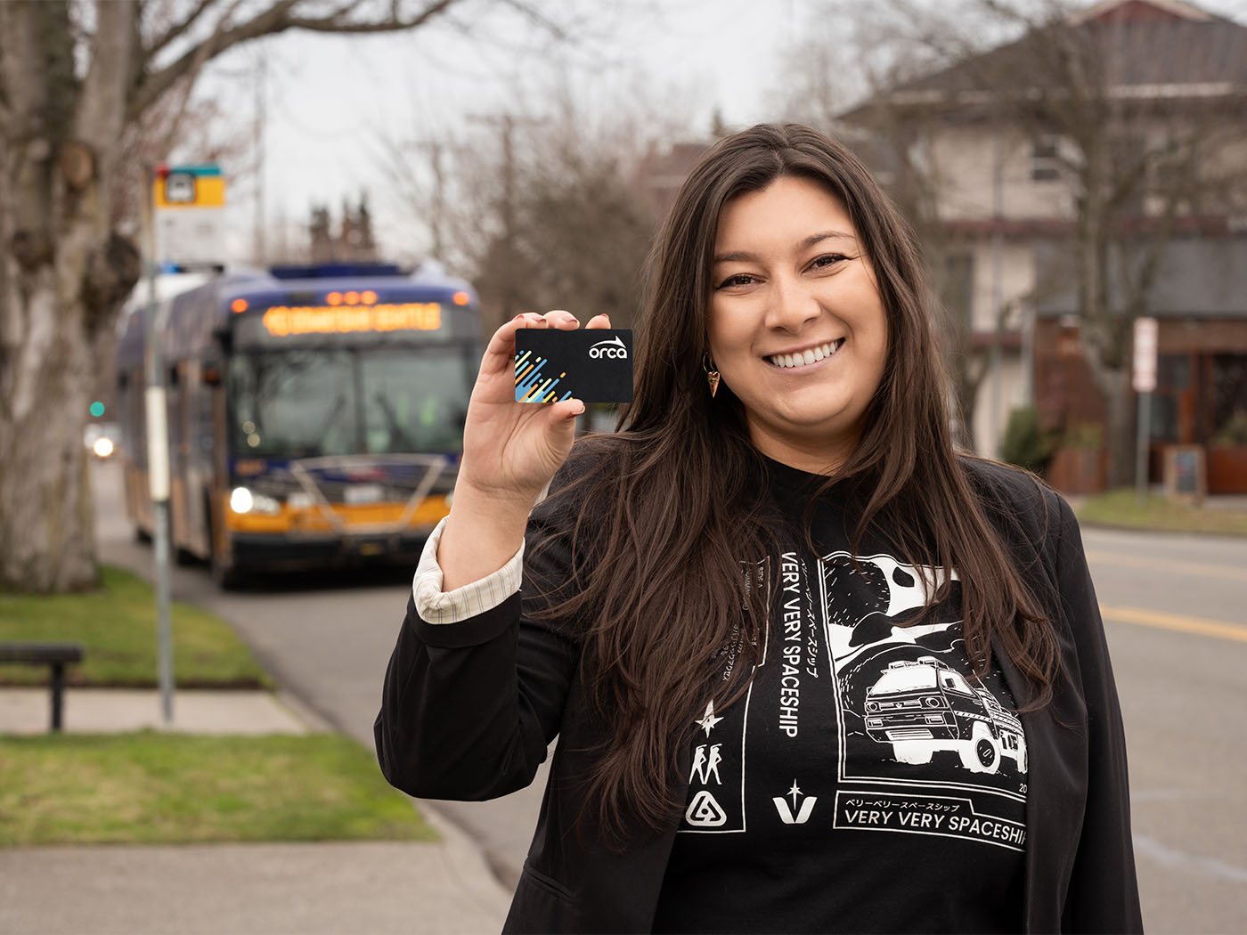Smiling woman holding up an ORCA card. Bus in background.