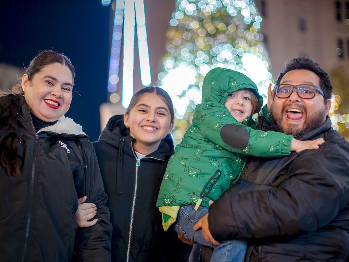 Family smiling in front of holiday lights