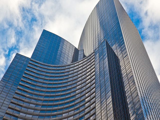 Buildings against a blue sky with white clouds reflecting on the windows